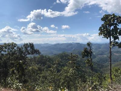 Uitzicht over groene bergketens en bos in Thailand onder een blauwe lucht met wolken.