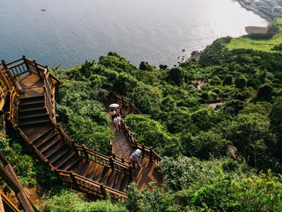 Houten trap en wandelpad langs de groene kliffen van Jeju-do met uitzicht op zee, Zuid-Korea.