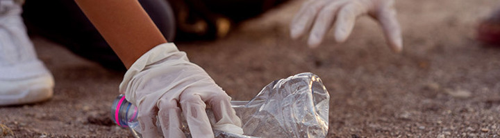 Handschoenen rapen een plastic fles op van de grond tijdens een opruimactie, als duurzame reistip.