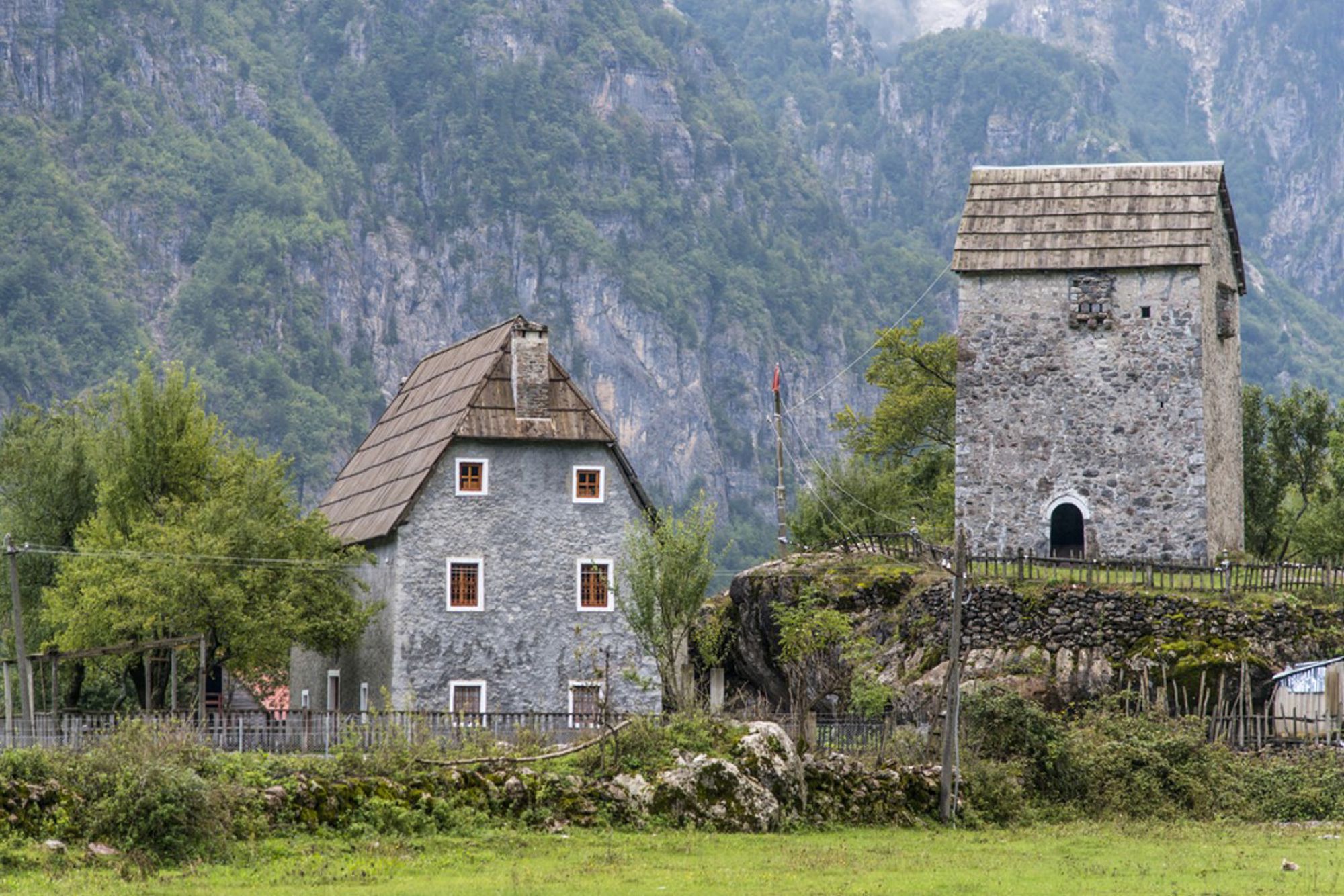 Traditioneel stenen huis en verdedigingstoren in de Albanese Alpen, omringd door groene bergen.