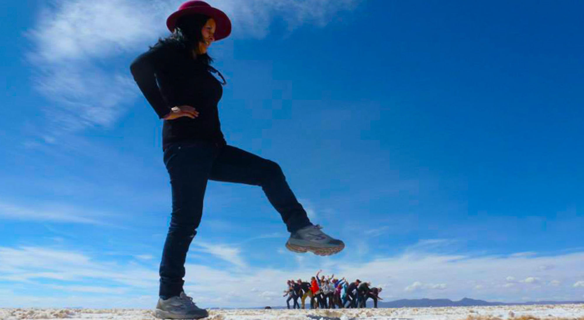 Perspectieffoto van een vrouw met hoed die lijkt te stappen over een groep mensen op een zoutvlakte.