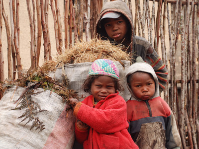 Kinderen op Madagascar bij een houten omheining met zakken vol hooi en takken.