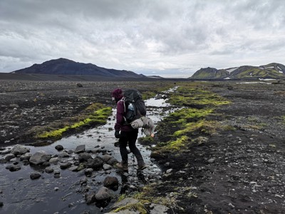 Wandelaar steekt een beekje over in het ruige IJslandse hoogland tijdens de Laugavegur Trail.