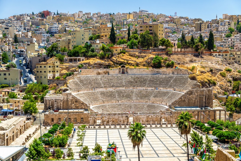 Romeins amfitheater in Amman, Jordanië, met tribunes en stadswijk op de achtergrond.