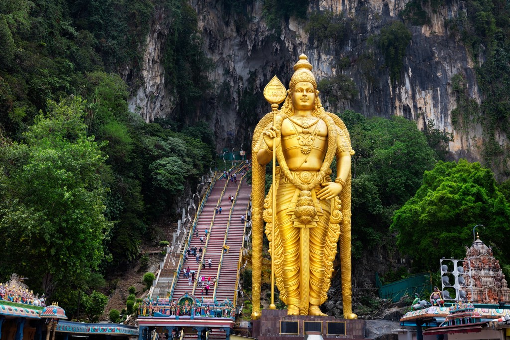Gouden Murugan-beeld bij de Batu Caves, Maleisië, met kleurrijke trappen naar de grotten in de kalksteenrotsen.