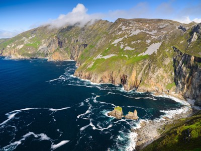 Groene kliffen langs de Atlantische kust van Ierland, met schuimende golven en rotsen in zee.