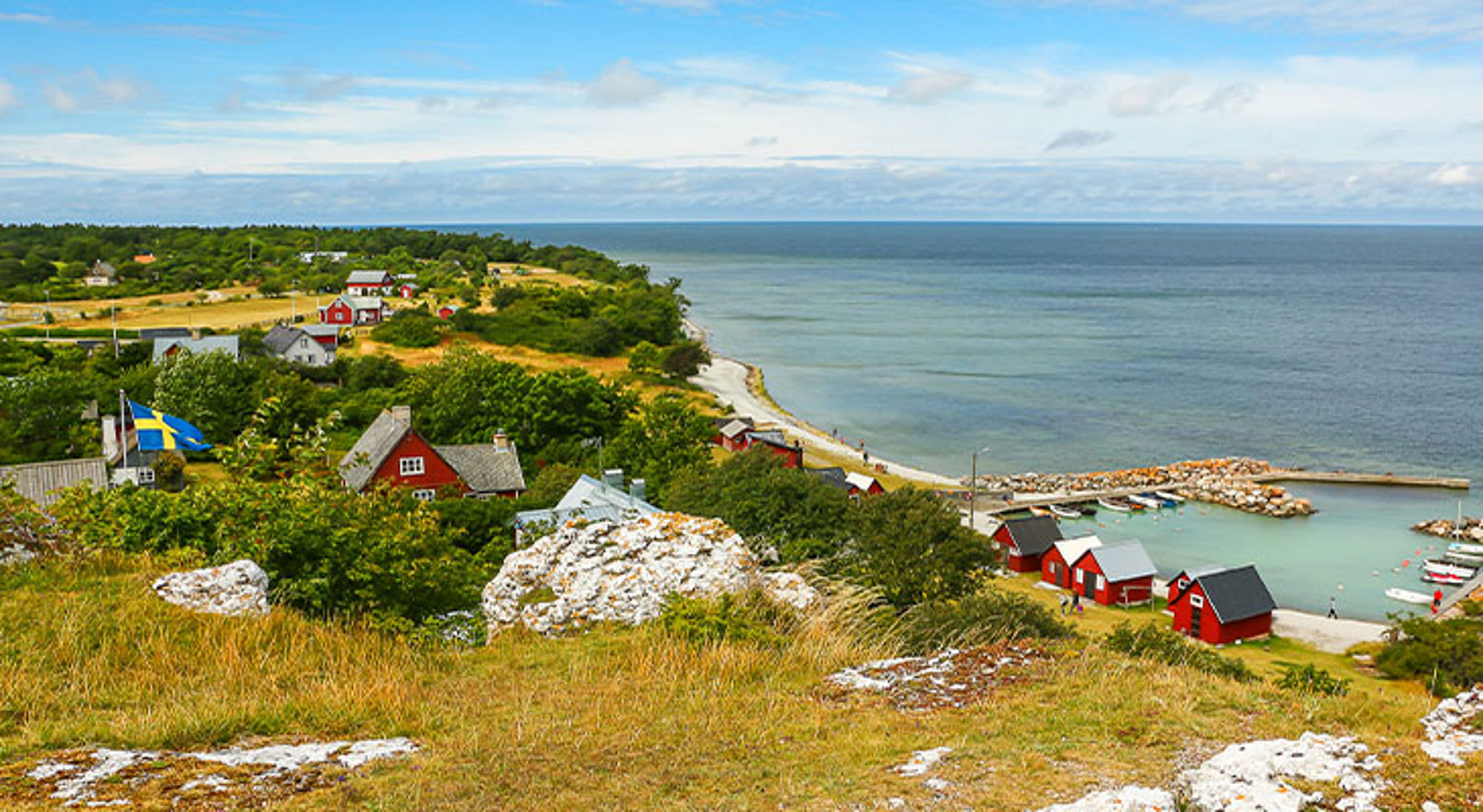 Gotland Uitzicht op een Zweeds kustdorp met rode huisjes, kleine haven en strand aan de Baltische Zee.