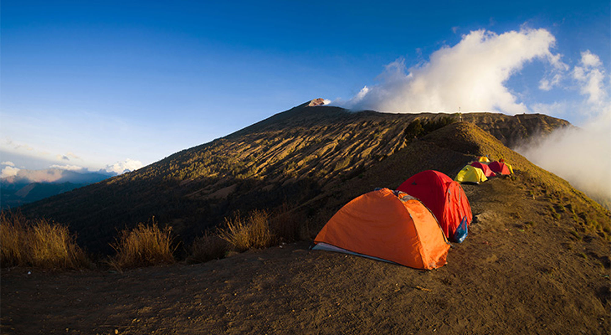 Rinjani-vulkaan Indonesië Tenten op een bergkam tijdens een trekking bij zonsopkomst, met wolken boven de vulkaankrater.