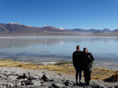 Reizigers aan de oever van een hooggelegen lagune met besneeuwde Andesbergen tijdens de route Bolivia en Chili.