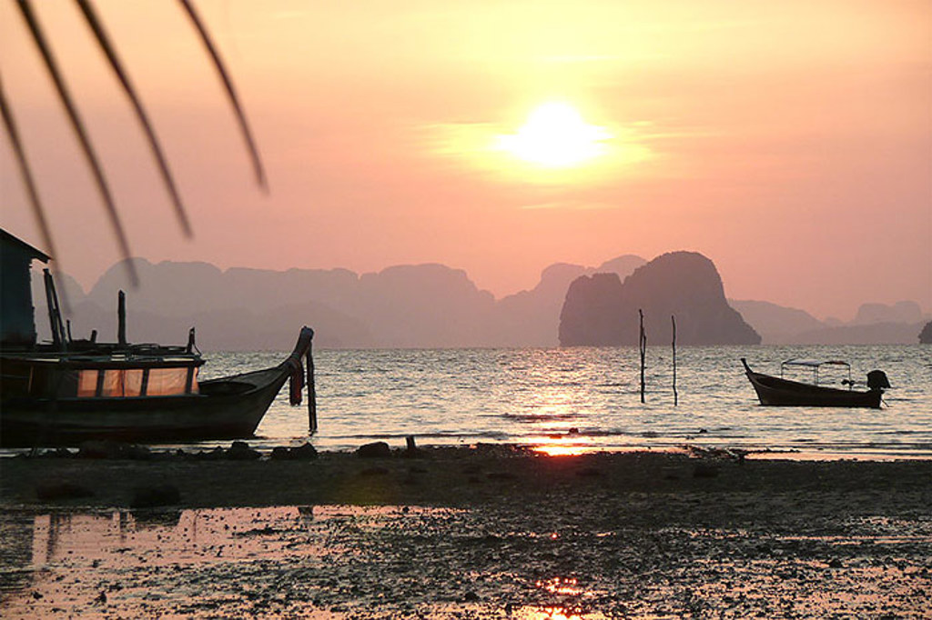 Zonsondergang aan zee in Zuid-Thailand met longtailboten en eilandrotsen op de achtergrond.