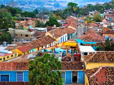 Uitzicht over kleurrijke huizen en rode dakpannen in Trinidad, Cuba, met groene heuvels op de achtergrond.
