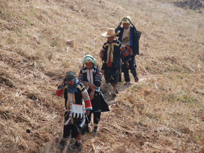Wandelaars in traditionele kleding lopen over een pad door droog grasland in Thailand.
