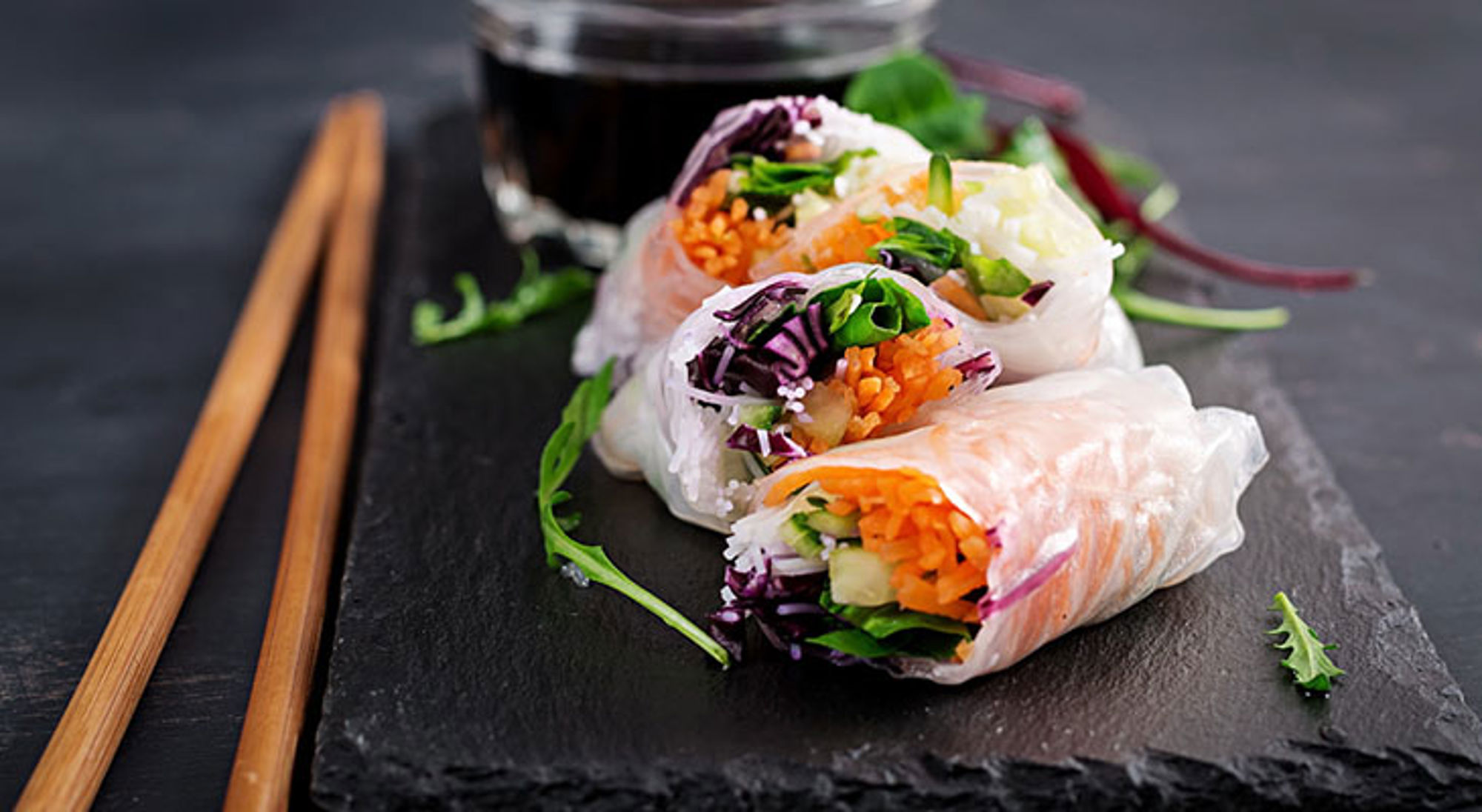 Vegetarisch Vietnamees gerecht Verse Vietnamese springrolls met groenten op een leisteenplank, met eetstokjes en dipsaus.