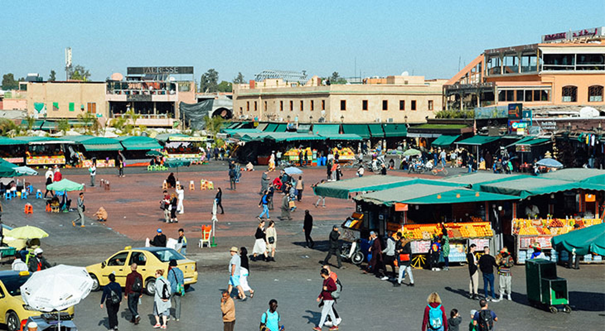 Djemaa El Fna plein Drukke markt op het Djemaa el Fna-plein in Marrakech met kraampjes, taxi’s en bezoekers.