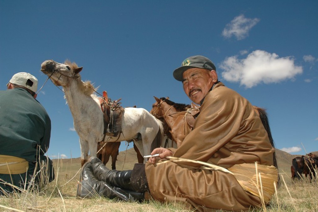 Mongoolse herder zit in de steppe bij paarden onder een blauwe lucht tijdens een groepsrondreis Mongolië.