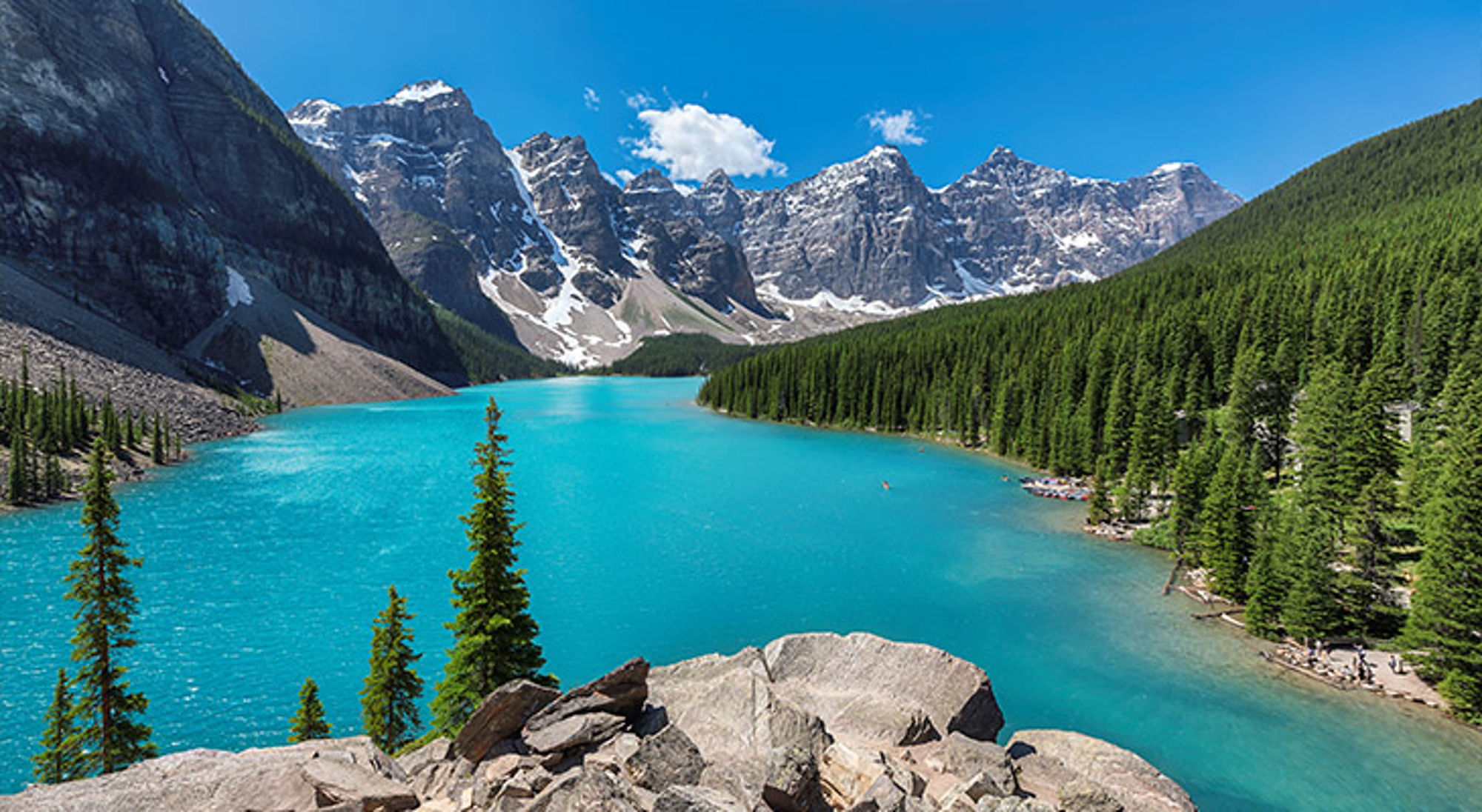 Canada Turquoise bergmeer met dennenbos en besneeuwde bergtoppen onder een blauwe lucht.