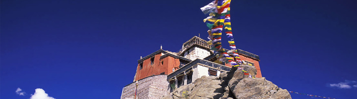 Boeddhistisch klooster op rots met wapperende gebedsvlaggen in Ladakh.