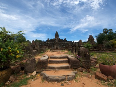 Stenen tempelruïne bij Angkor in Cambodja, met trappen en een pad naar de centrale toren onder blauwe lucht.