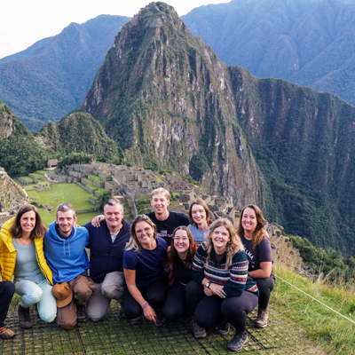 Groepsfoto van 22-35ers reis Peru bij Machu Picchu, met de ruïnes en bergen op de achtergrond.