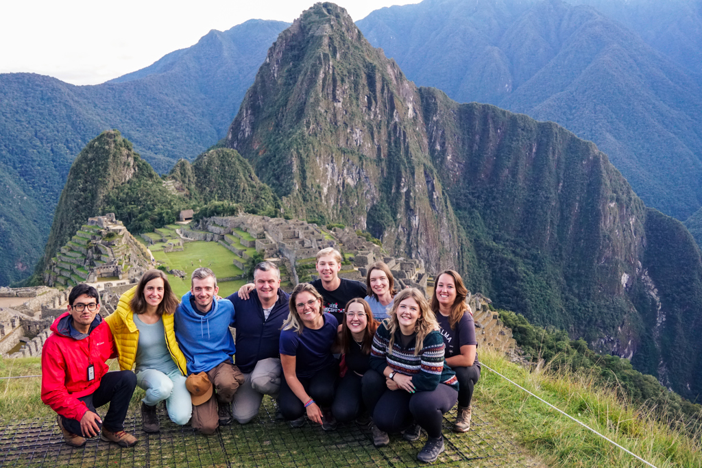 Groepsfoto van 22-35ers reis Peru bij Machu Picchu, met de ruïnes en bergen op de achtergrond.