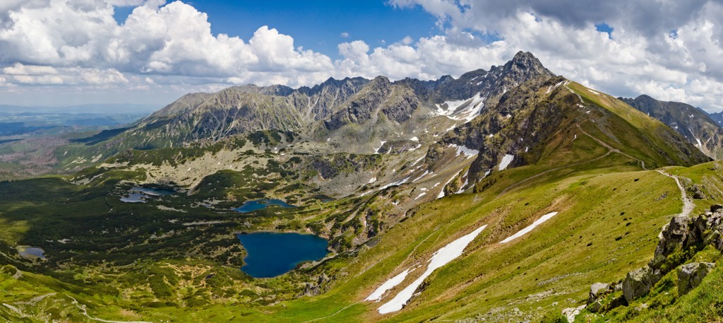Berglandschap in de Poolse Tatra met bergmeren, groene hellingen en besneeuwde pieken onder een blauwe lucht.