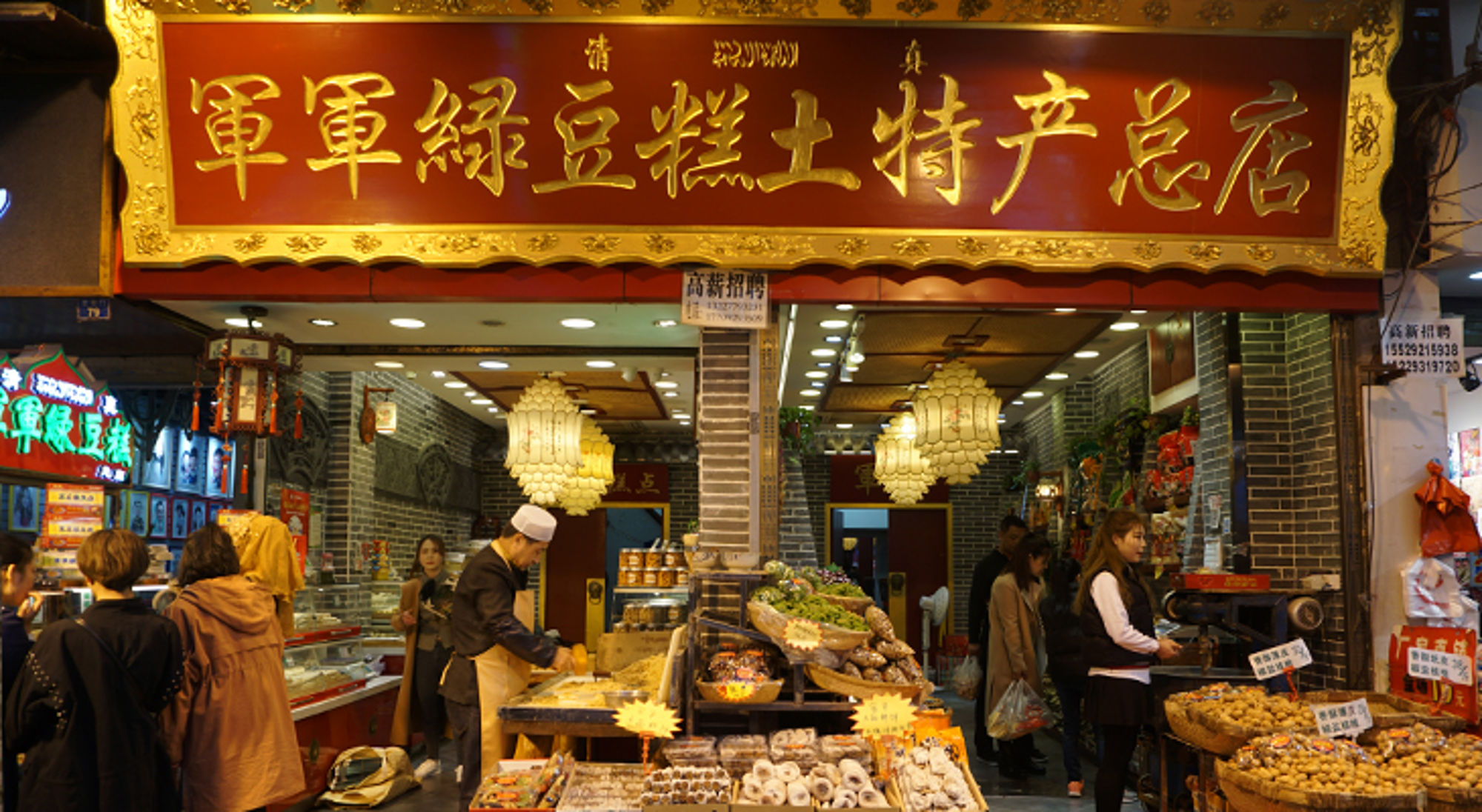 Straatkraam met Chinese lekkernijen onder rood-gouden uithangbord en lampionnen, met klanten in de winkel.