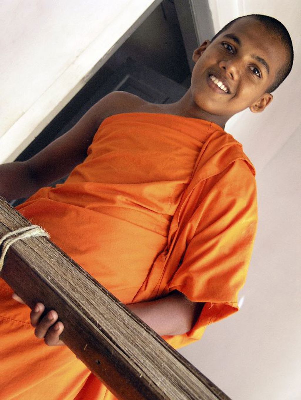 Jonge boeddhistische monnik in oranje gewaad in Myanmar, glimlachend op een houten trap.