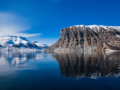 Besneeuwde bergen en steile rotswand weerspiegeld in het stille fjordwater van Spitsbergen.