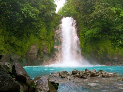 Waterval in het regenwoud van Costa Rica met turquoise rivier en rotsen.
