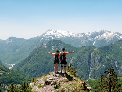 Wandelaars met rugzak op bergtop met uitzicht op de Balkanbergen en besneeuwde pieken tijdens Route Balkan.