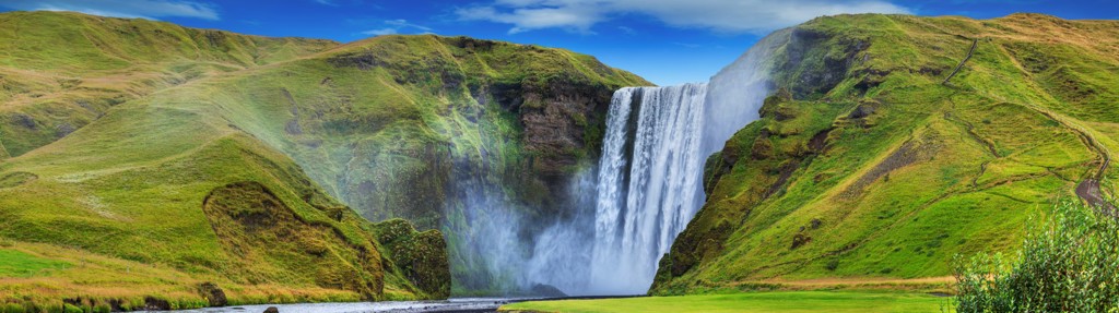 Skógafoss-waterval in IJsland, omringd door groene heuvels tijdens een groepsrondreis.