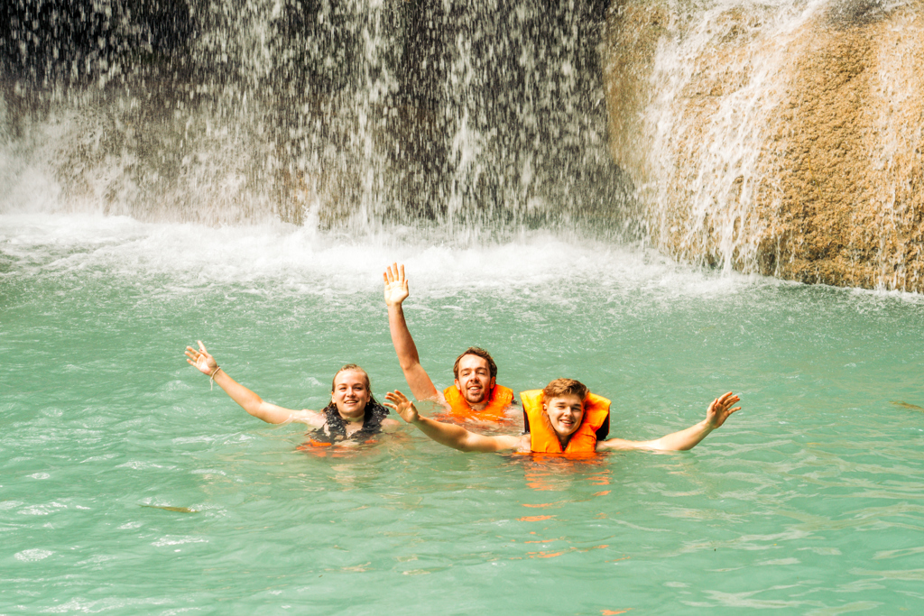 Jongeren zwemmen met reddingsvesten bij een waterval tijdens een 22-35ers reis in Thailand.