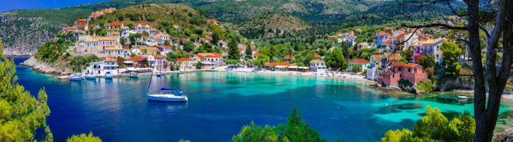 Kleurrijk kustdorp aan een turquoise baai met zeilboten op Kefalonia, Griekenland.