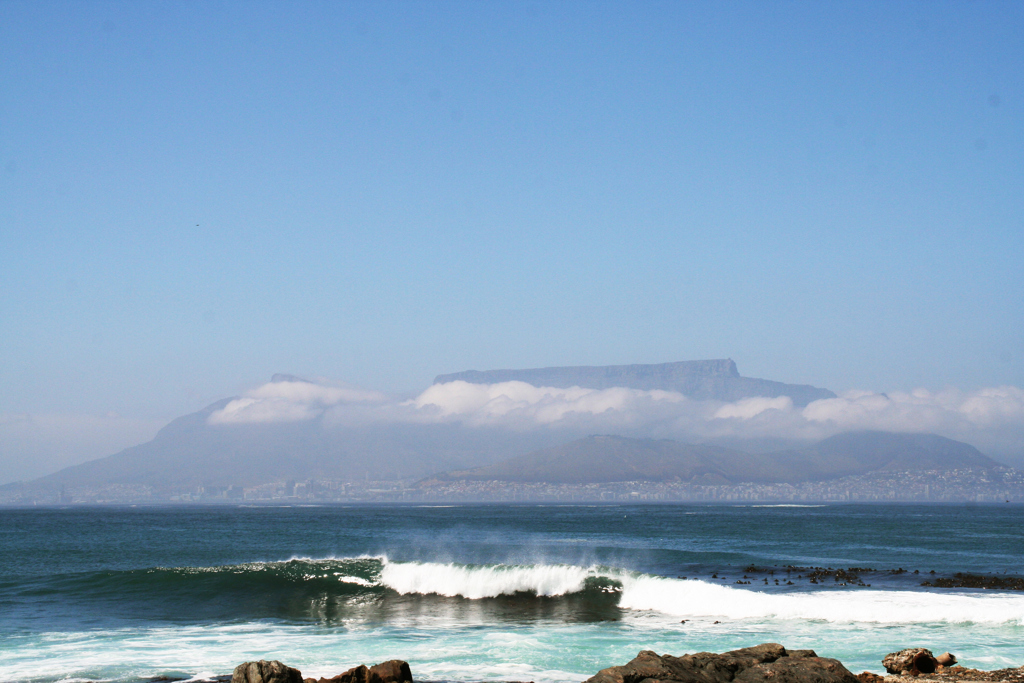 Golven aan de kust met op de achtergrond de Tafelberg bij Kaapstad, Zuid-Afrika.