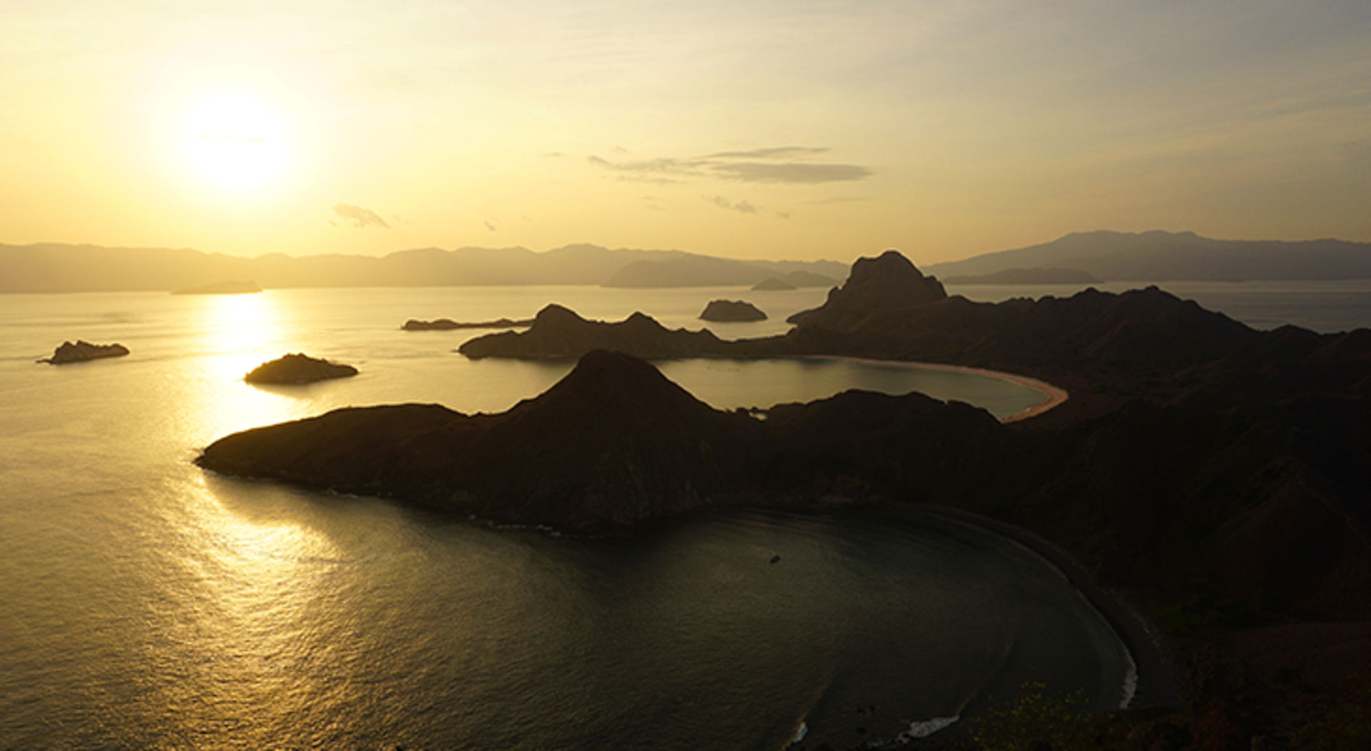 uitzicht over de zee - komodo eilanden Zonsondergang boven de Komodo-eilanden met bergachtige kustlijn en baaien, Indonesië.