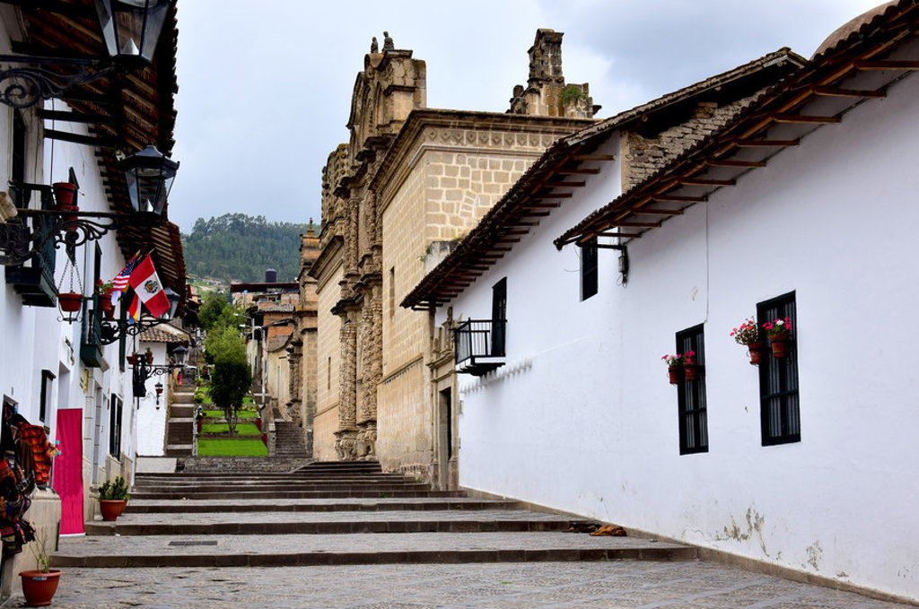 Straat met witte huizen en kerk in Cajamarca, Noord-Peru, met Peruaanse vlaggen en bloemen aan gevels.