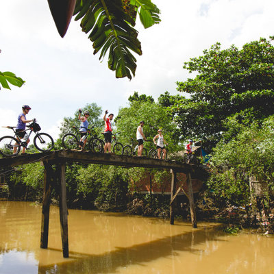 Fietsers op een smalle houten brug over een rivier tijdens fietsvakantie Vietnam, Cambodja en Thailand.