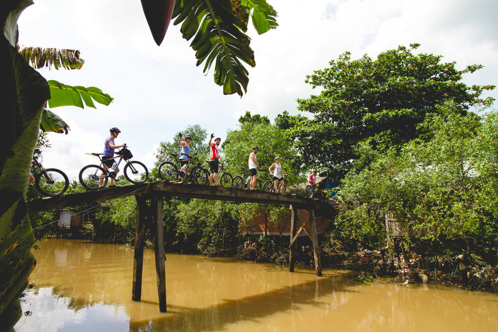 Fietsers op een smalle houten brug over een rivier tijdens fietsvakantie Vietnam, Cambodja en Thailand.