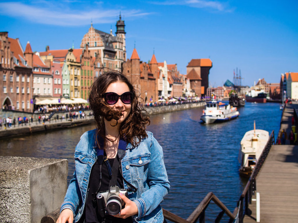 Vrouw met camera aan de rivier in Gdańsk, met historische gevels en boten tijdens familiereis Polen en Baltische Staten.