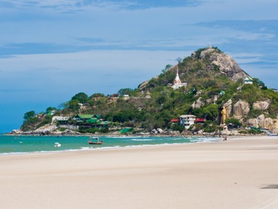 Zandstrand met uitzicht op Khao Takiab bij Hua Hin, Thailand, met tempel op de heuvel en boten op zee.