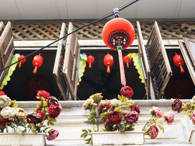 Rode Chinese lantaarn bij houten luiken en bloemen aan een gevel in Singapore, Maleisië of Thailand.