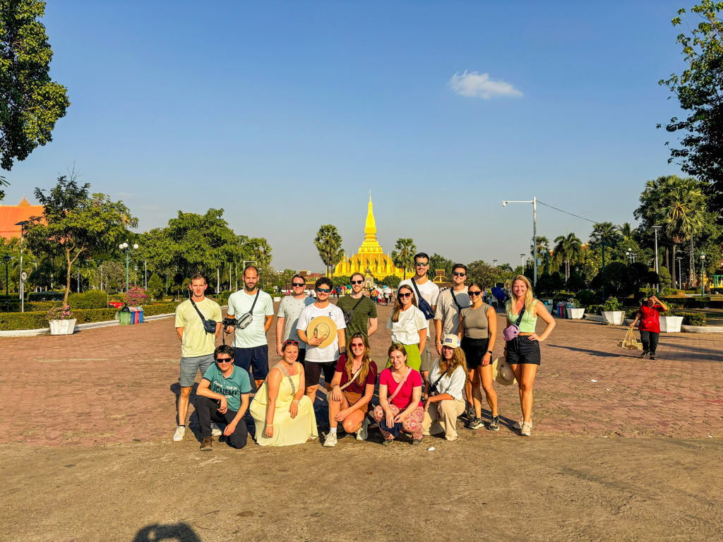 Groepsfoto van 22-35ers tijdens reis Thailand, Laos en Cambodja, met Pha That Luang in Vientiane op de achtergrond.