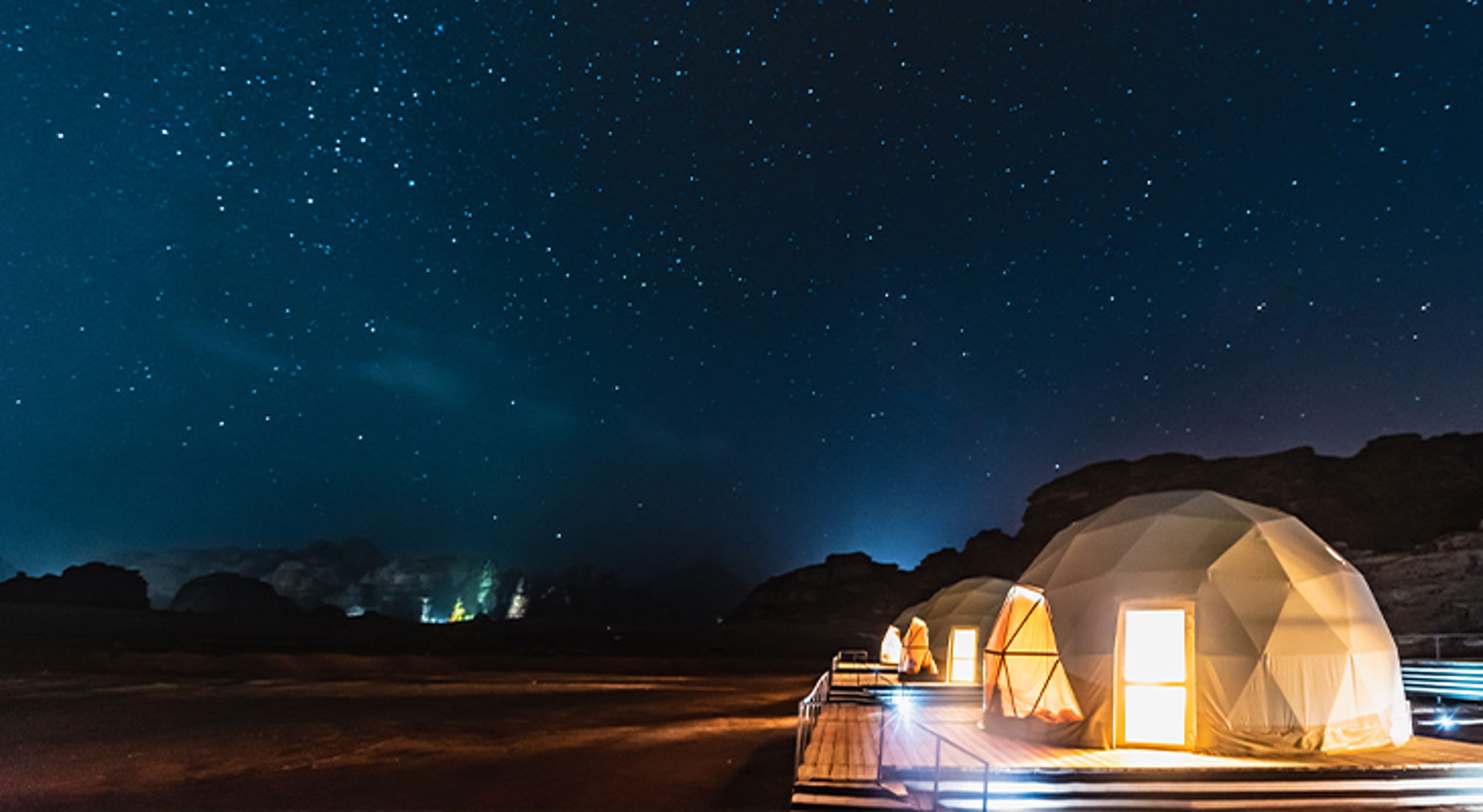Wadi Rum Jordanië Verlichte koepeltenten onder een heldere sterrenhemel in een donker landschap.