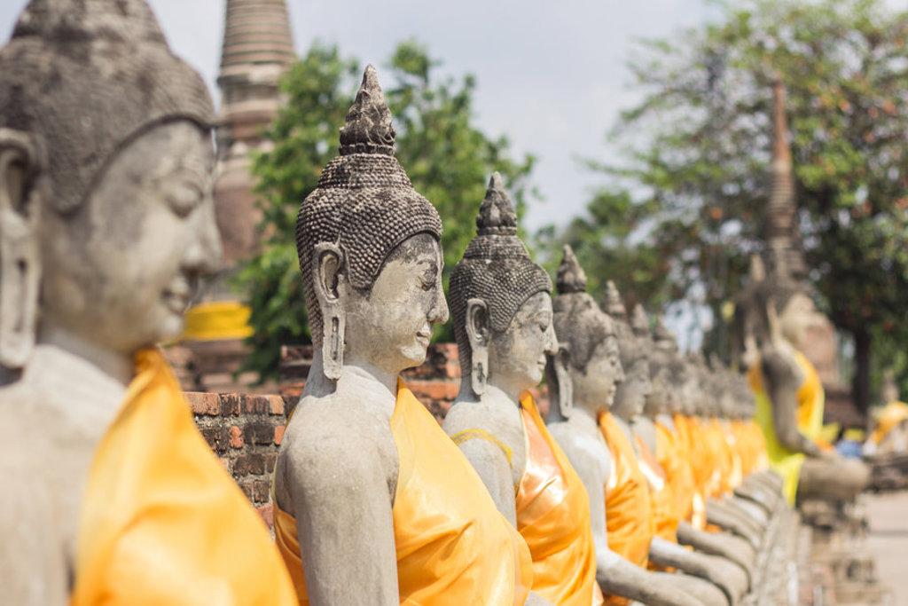 Rij boeddhabeelden met oranje gewaden bij een tempelcomplex in Thailand.