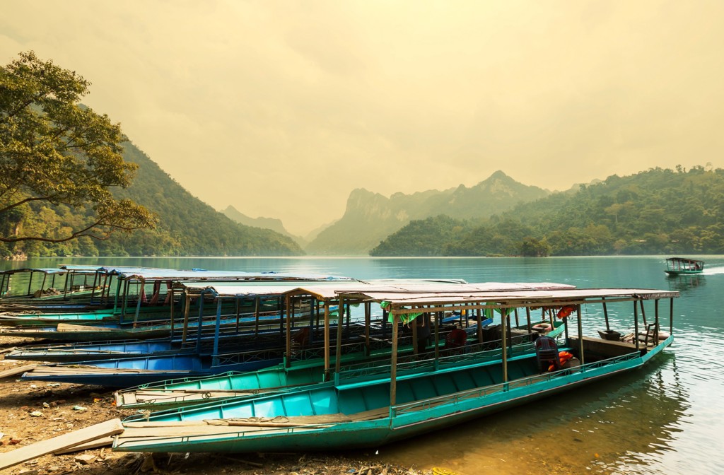 Longtailboten aan de oever van een bergmeer in Vietnam tijdens een groepsrondreis, met groene heuvels op de achtergrond.