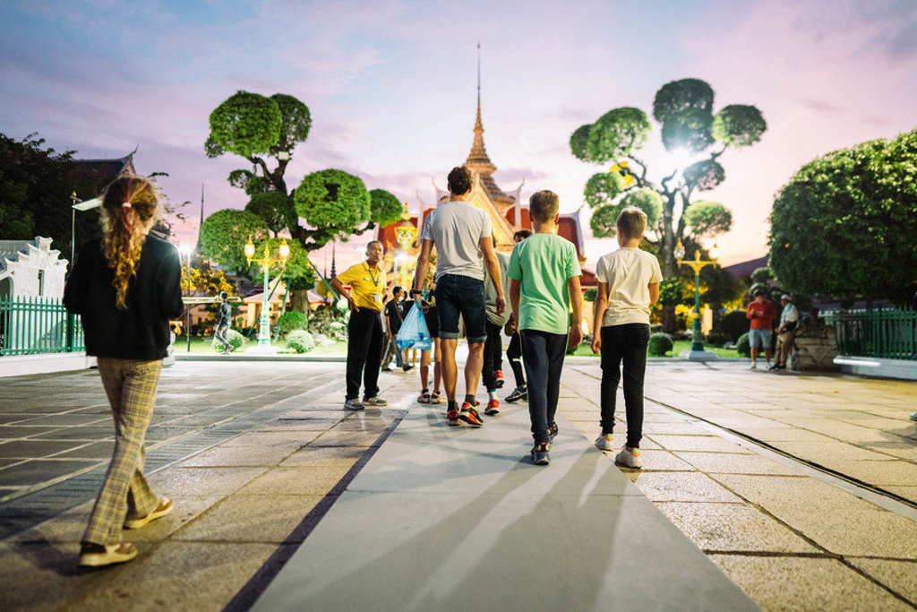 Gezin wandelt bij avondlicht naar een verlichte tempel in Thailand tijdens een familiereis.