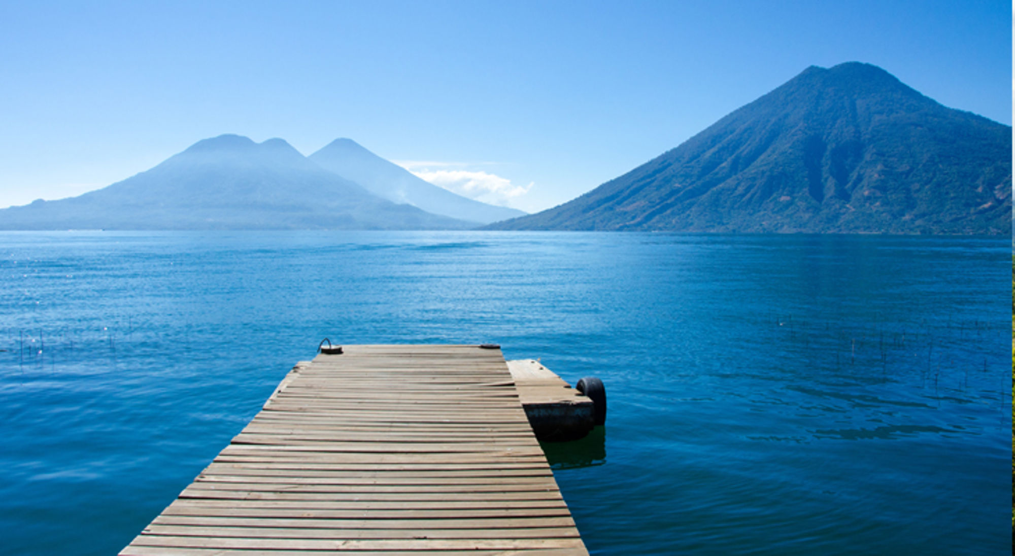 Meer van Atitlan in Guatemala Houten steiger aan een helderblauw meer met vulkanen op de achtergrond.