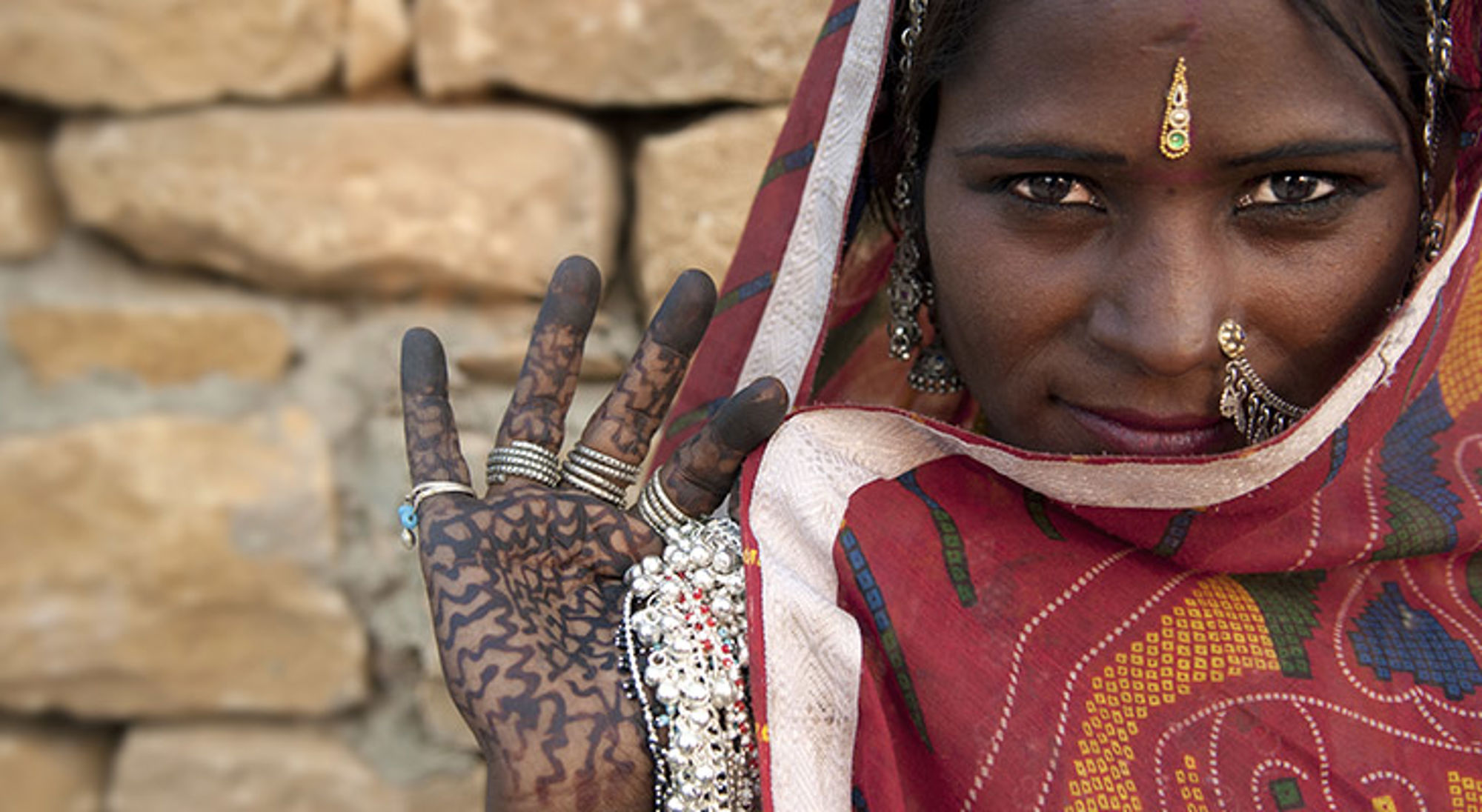 Portret van vrouw met traditionele sieraden en henna op haar hand, gehuld in een kleurrijke sjaal.