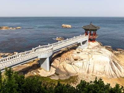 Haedong Yonggungsa-paviljoen op rotsen aan de kust van Zuid-Korea, bereikbaar via een witte brug.