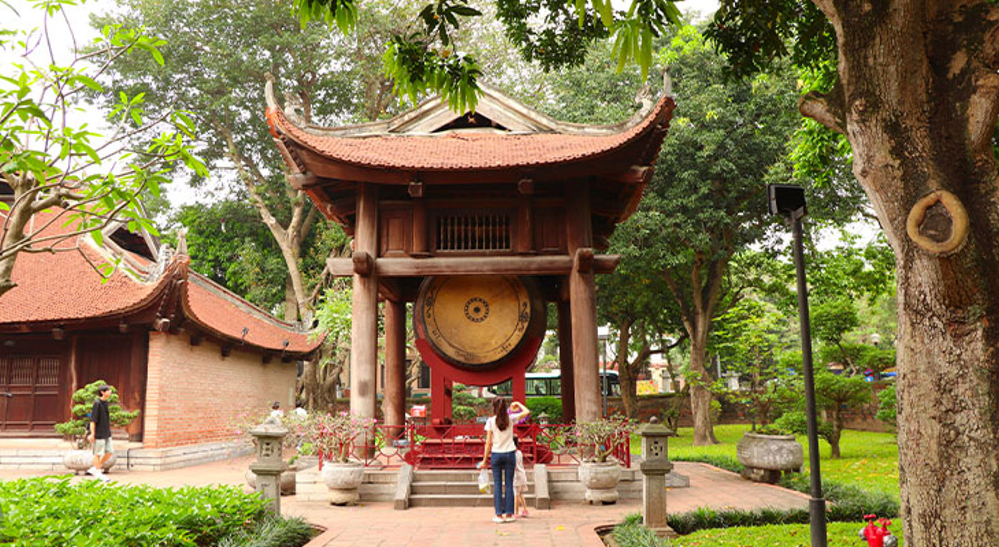 Hanoi Tempelcomplex met grote bronzen trommel en pagodedaken in een groene tuin.